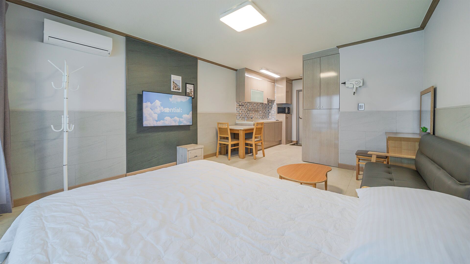 Habitación de hotel con cama, escritorio, silla, mesita, sofá, televisor y kitchenette.
