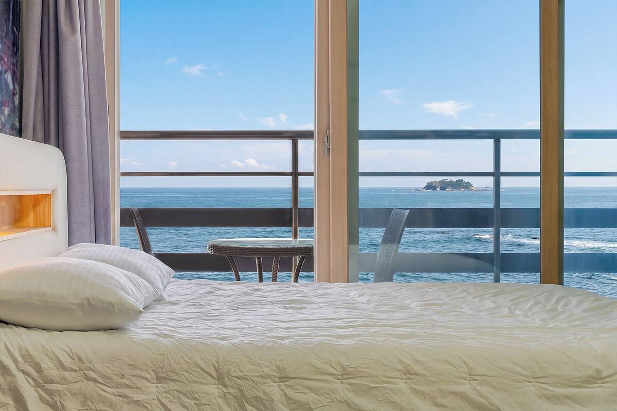 Una habitación de hotel con una cama, una mesita y vista al océano.