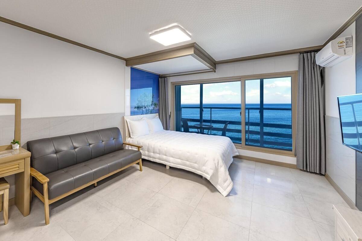 Una habitación de hotel moderna con cama, sofá, escritorio y un amplio ventanal con vistas al mar.