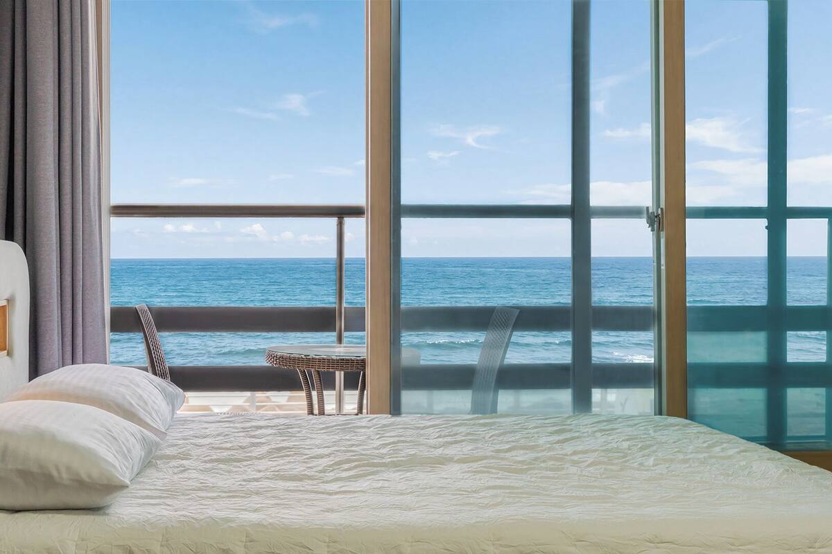 Un dormitorio con un ventanal grande, una cama, una silla y una mesita.