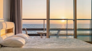 A bedroom with a large window overlooking the sea at sunset. - Sokcho Bird Island Pension (Sokcho)