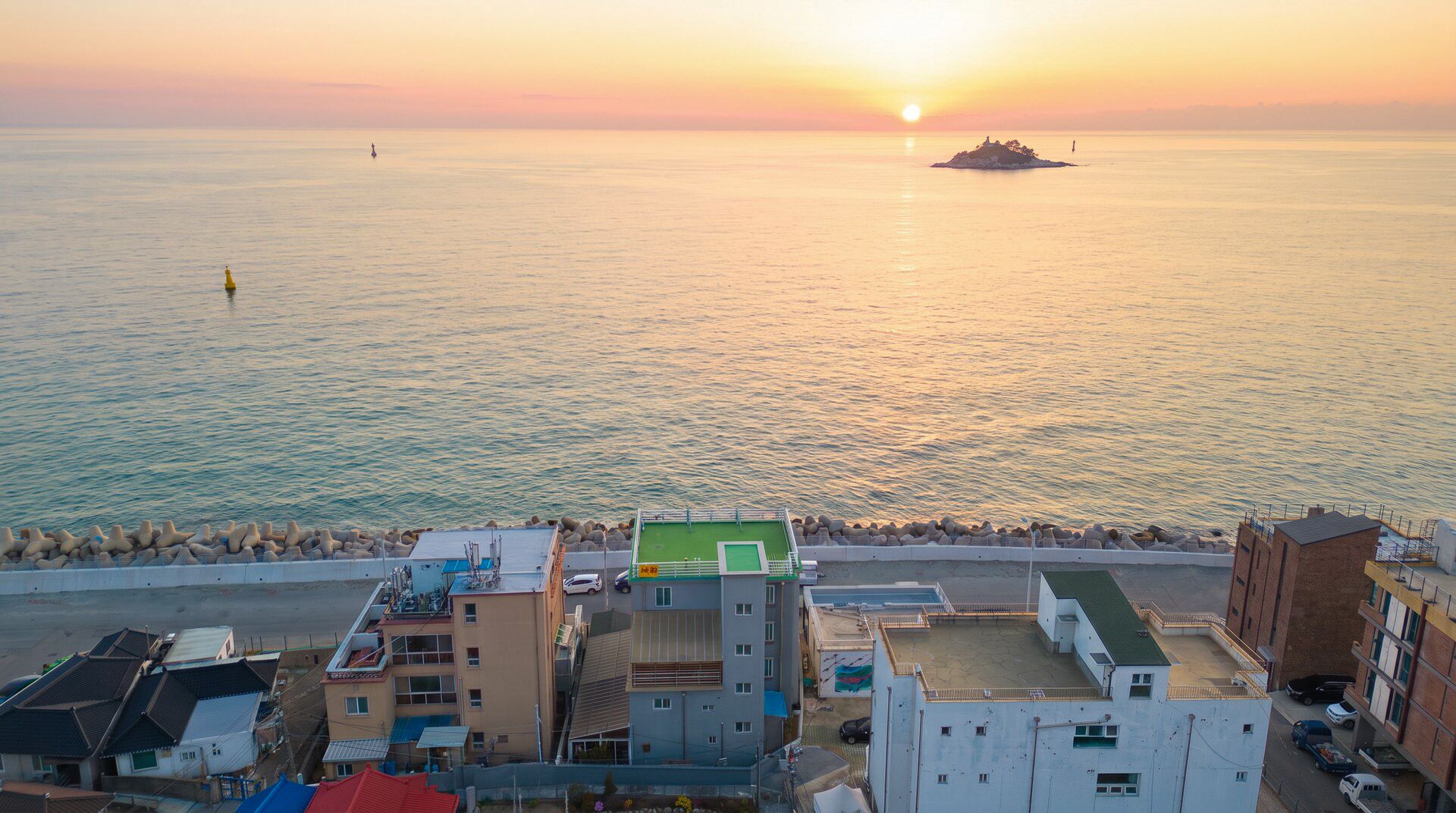 A coastal residential area with buildings, a pier, and a sunset over the sea.