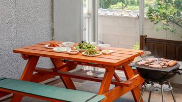 A wooden picnic table with food and a grill.