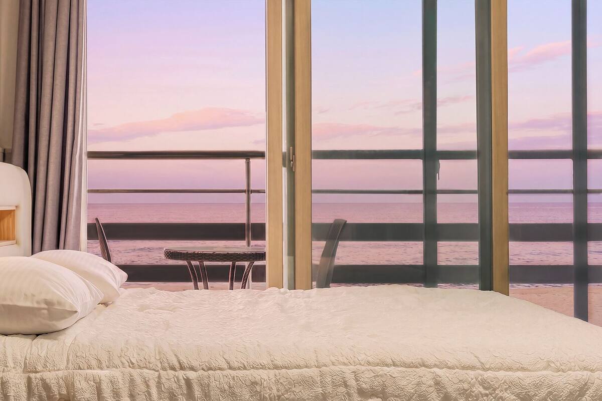 Un dormitorio con un ventanal grande, una cama, una mesita de noche y una silla.