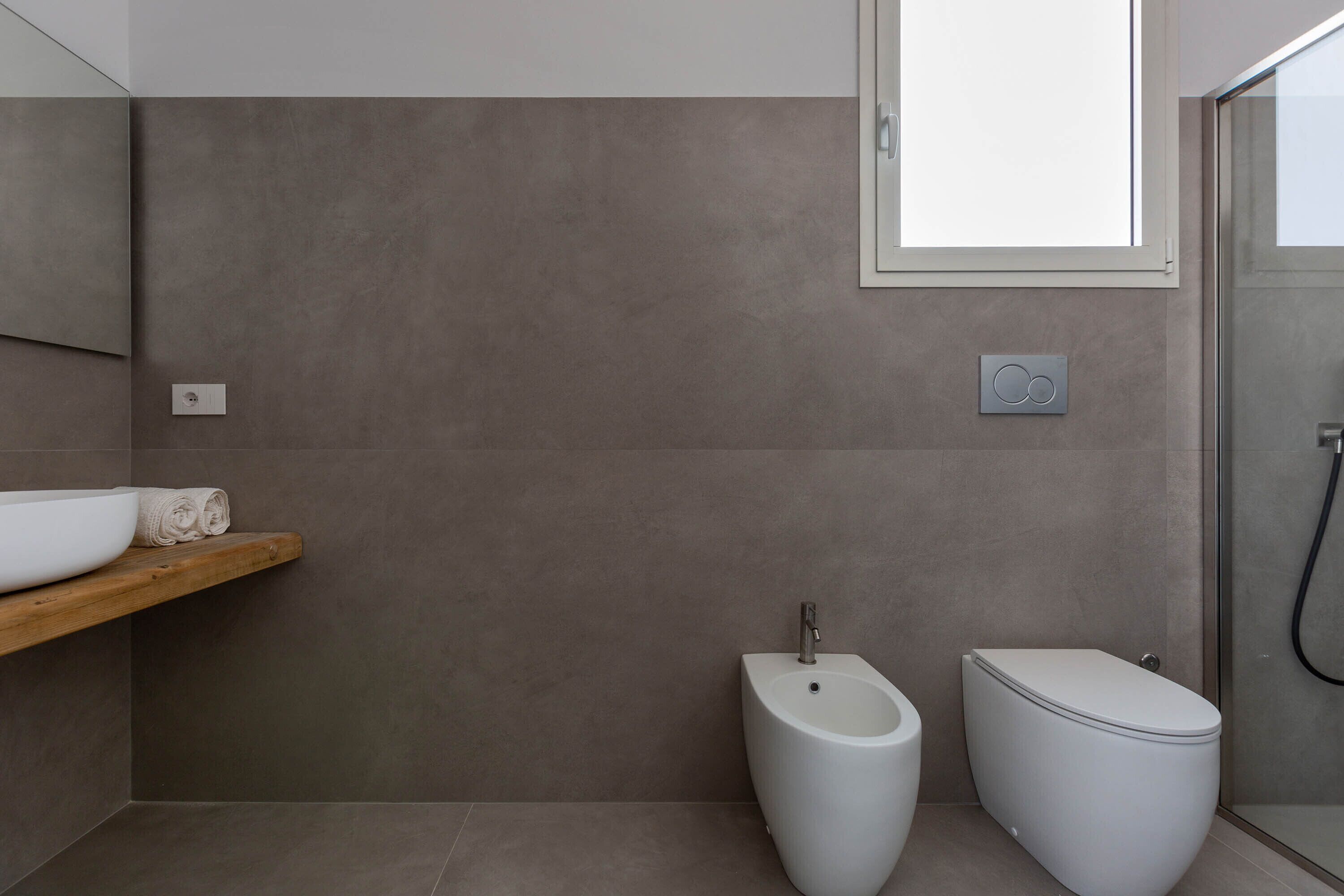 Un baño moderno con bidé, inodoro y una estantería de madera con lavabo blanco y toallas.
