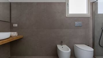 Un baño moderno con bidé, inodoro y una estantería de madera con lavabo blanco y toallas.