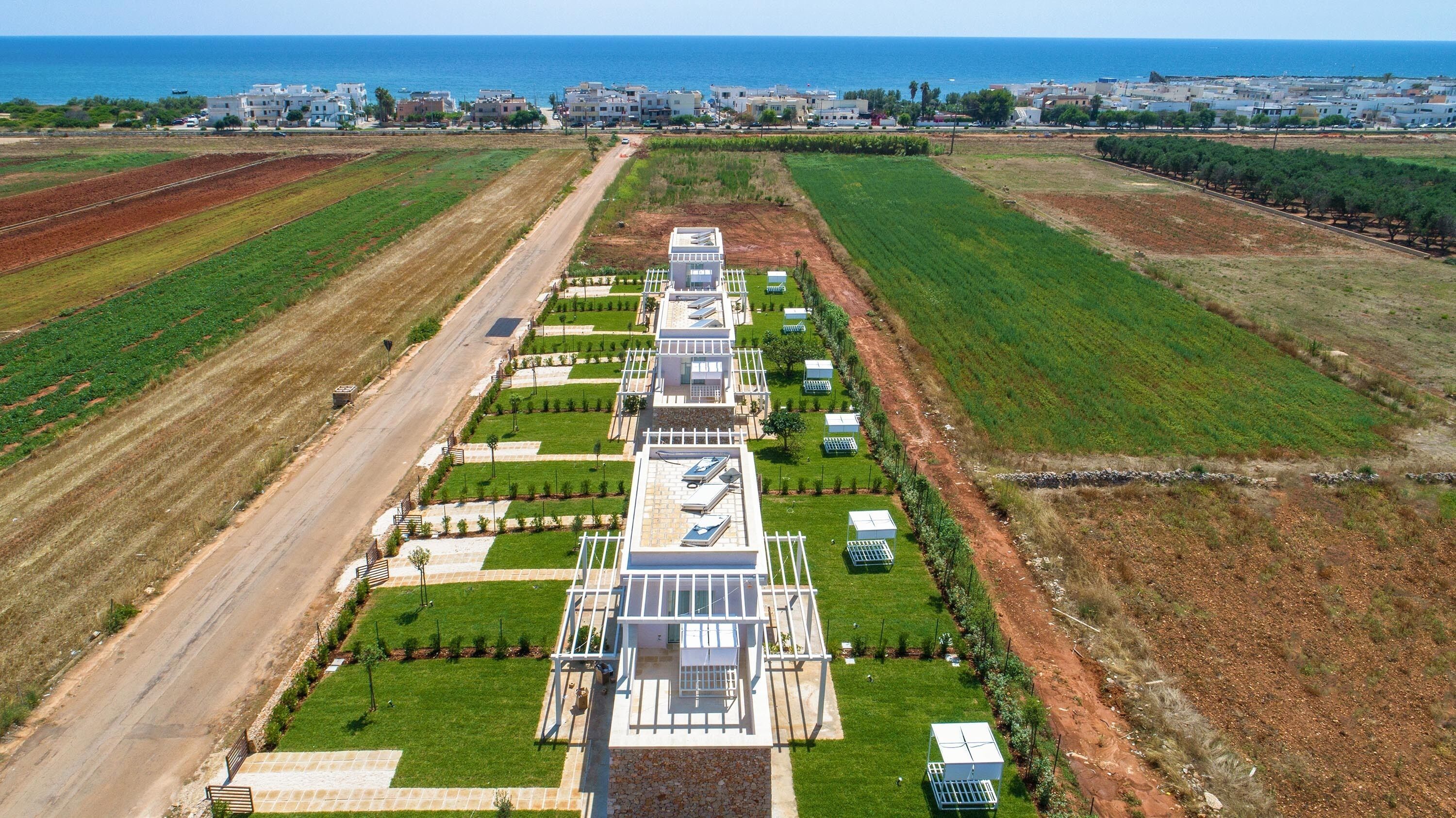 Um hotel moderno com um pátio central, rodeado por campos verdes e vista para o litoral.