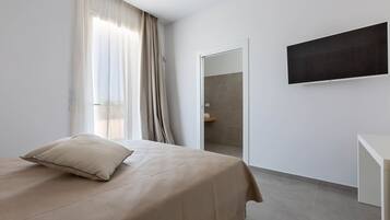 Habitación de hotel moderna con cama, televisión de pantalla plana, puerta que da a un baño y un ventanal con cortinas.