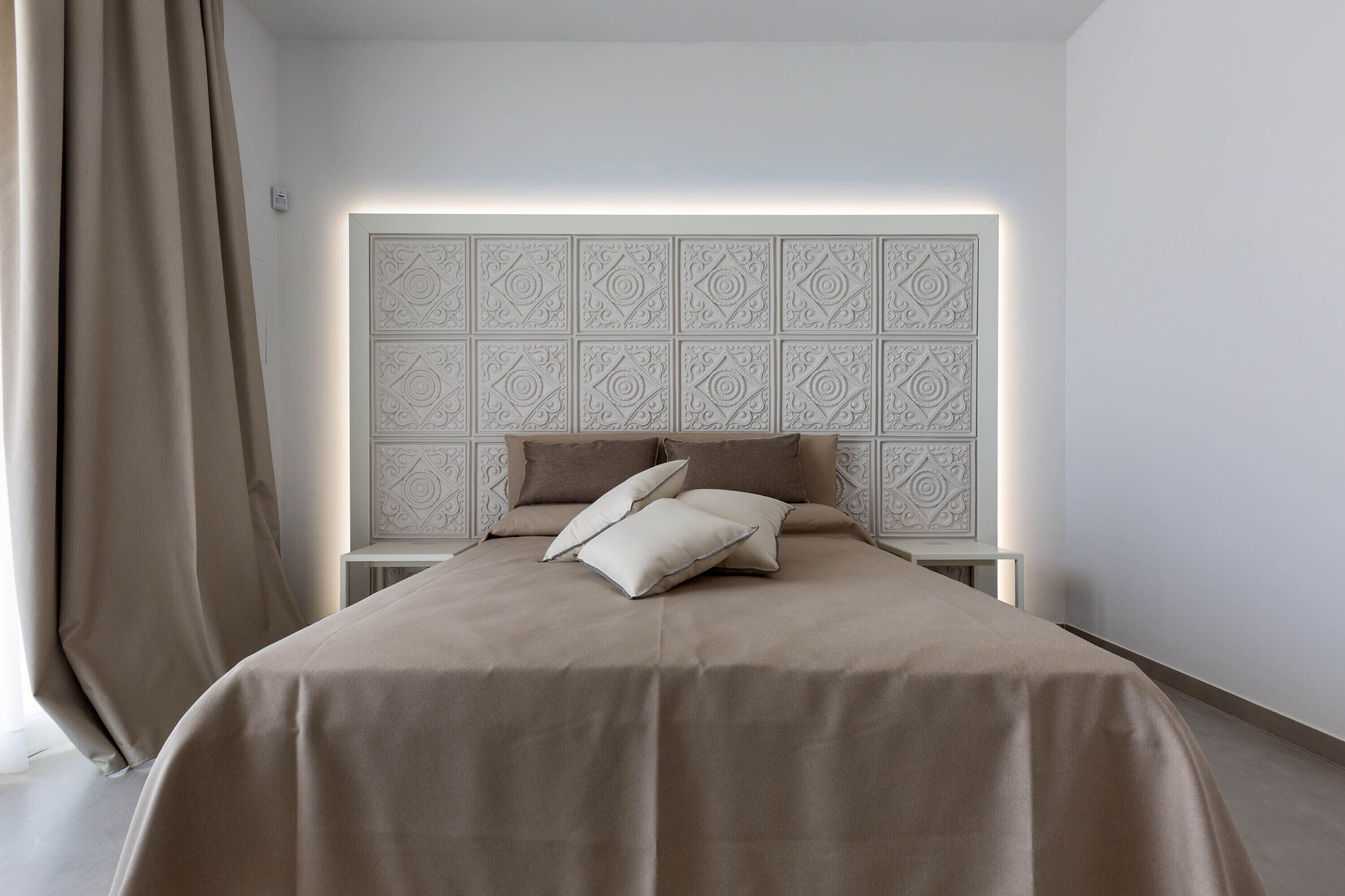 Een slaapkamer met een groot bed, een hoofdeinde met een geometrisch patroon en een raam met gordijnen.