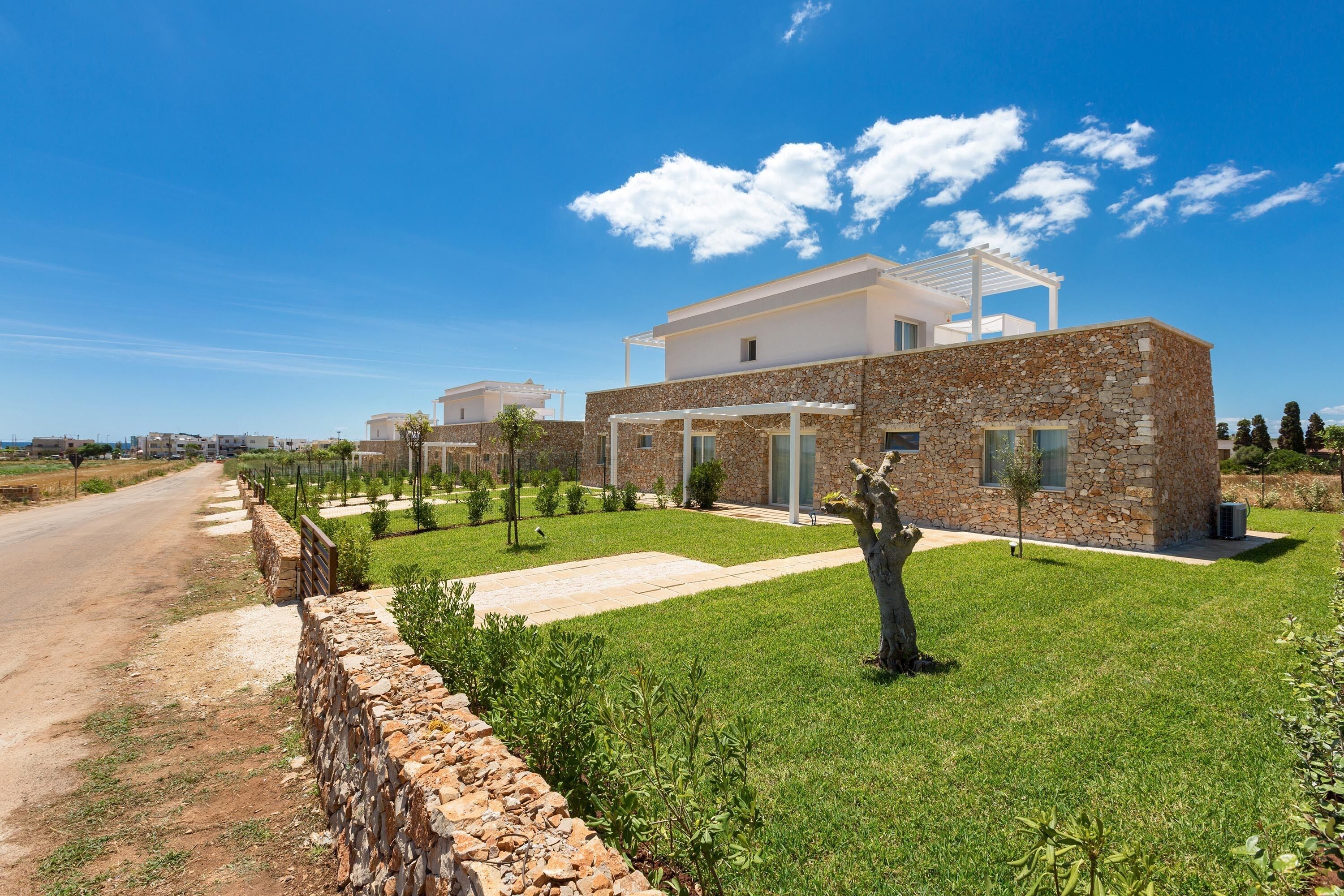 Una casa moderna con fachada de piedra, un porche blanco y un césped bien cuidado.
