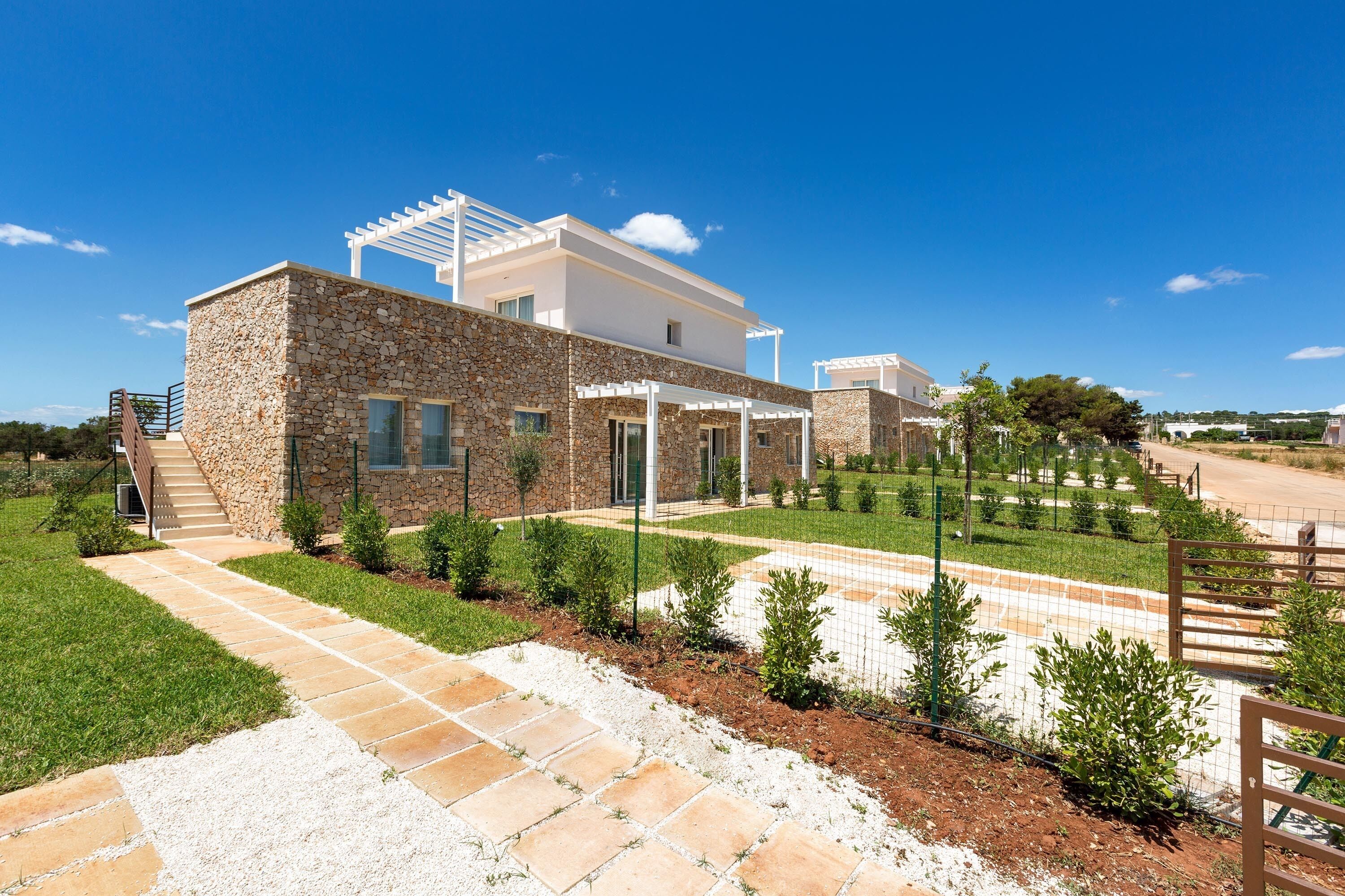 Une maison moderne avec une façade en pierre, un patio couvert et un jardin bien entretenu.