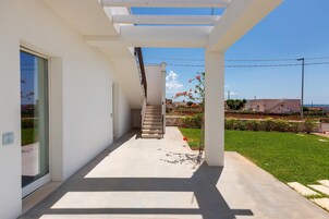 A modern house with a covered outdoor area, a staircase, and a view of the sea.