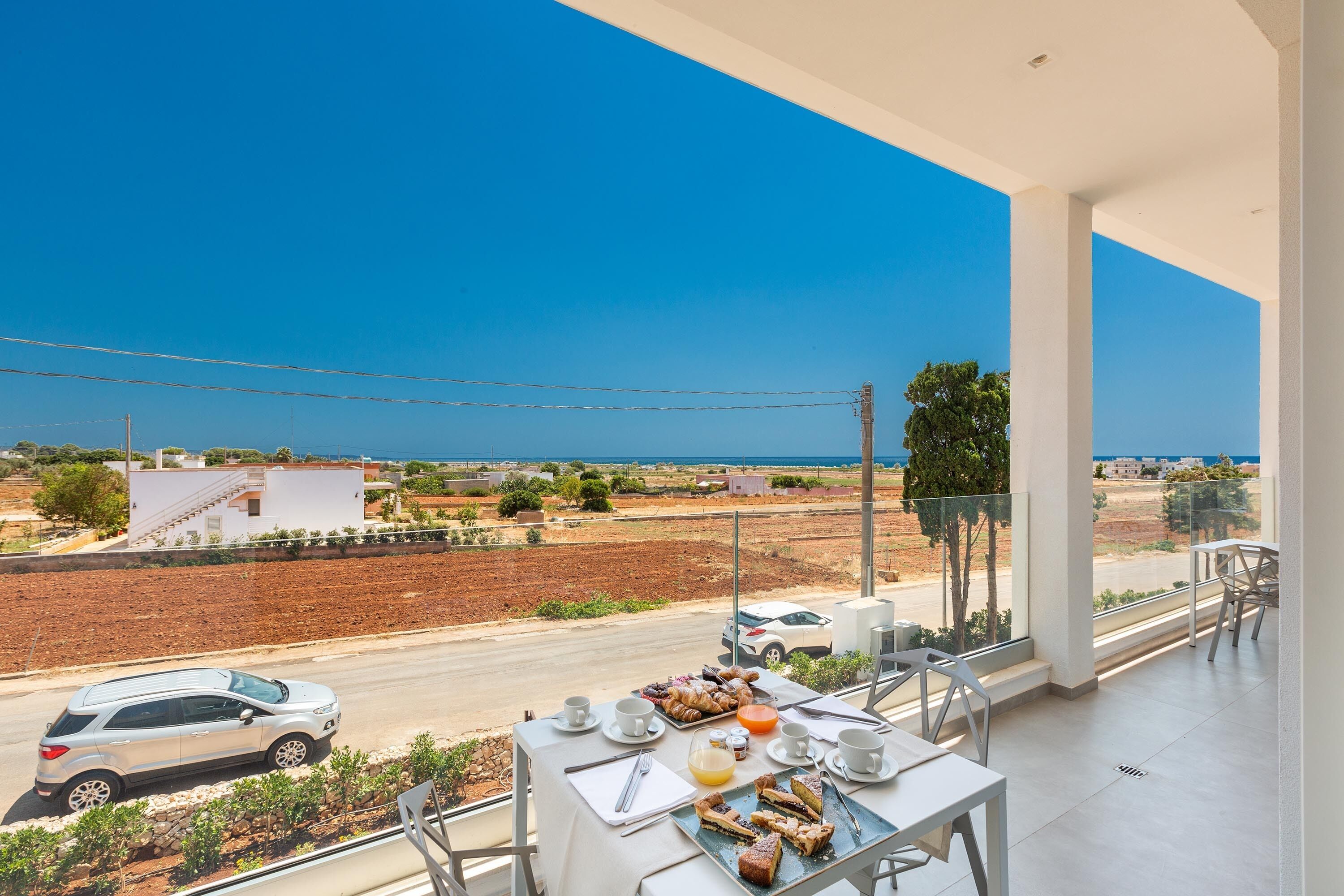A balcony with a table set for breakfast overlooking a coastal road.