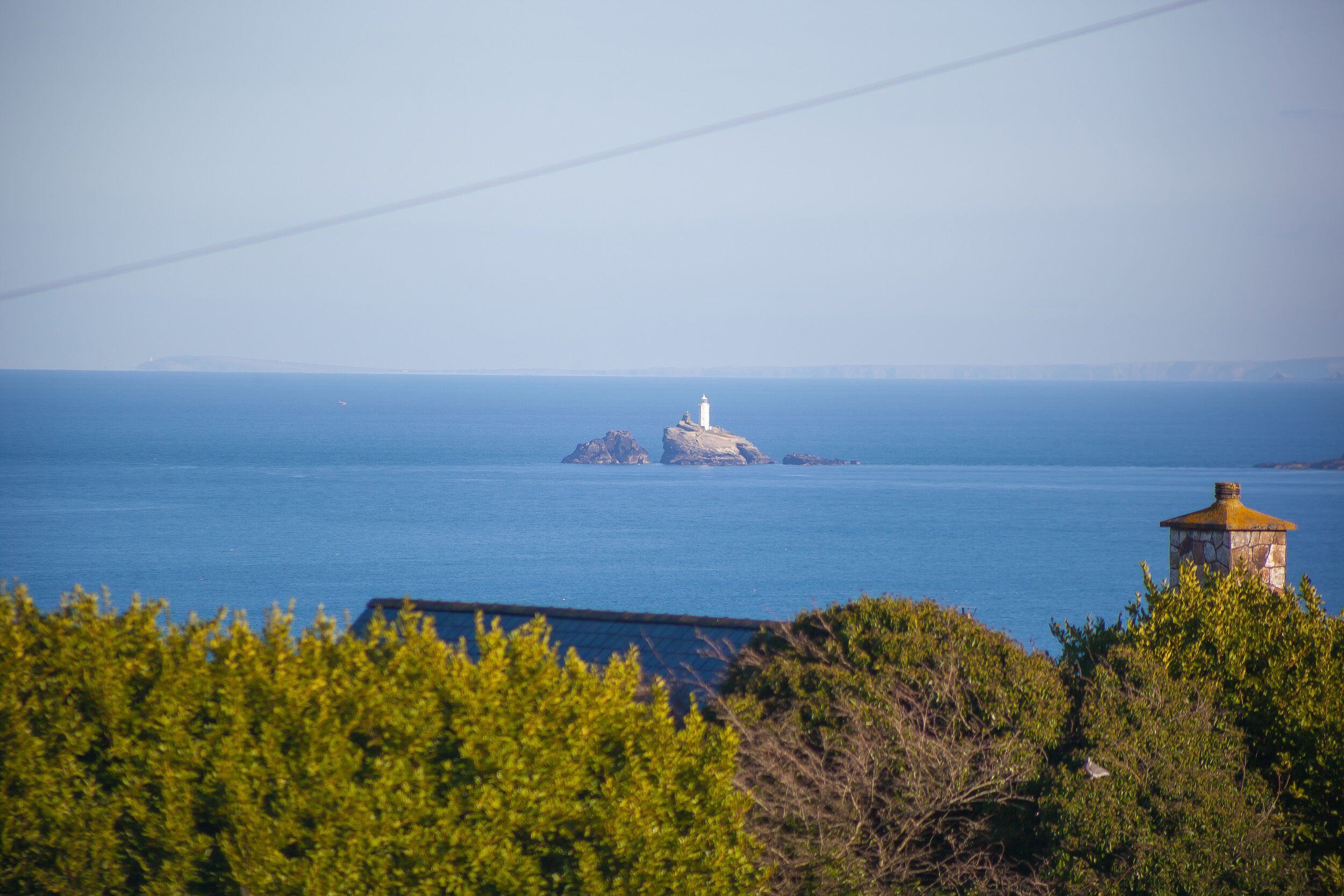 A lighthouse on a rocky outcrop surrounded by calm blue waters.