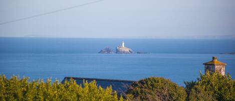 A lighthouse on a rocky outcrop surrounded by calm blue waters.