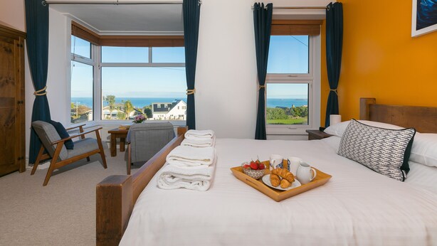 A hotel room with a bed, a chair, a small table, and a tray with breakfast items. - Oystercatcher House (St Ives)