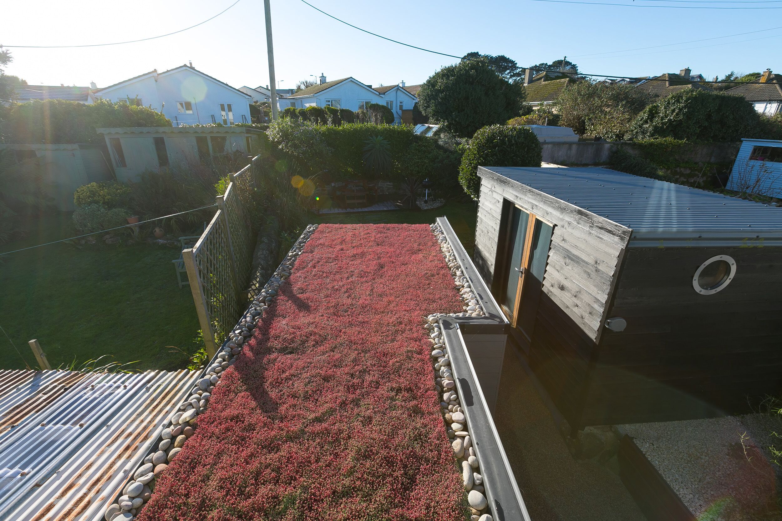 Eine Dachterrasse mit einem roten Blumenbeet, einer Holzkonstruktion und einem Metalldach.