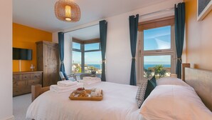 A hotel room with a large bed, a wooden wardrobe, a flat-screen TV, and a view of the sea. - Oystercatcher House (St Ives)