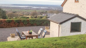 A house with a view of a lake and fields. There is a patio with a table and chairs. - Beech Tree Cottage (Caernarfon)