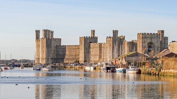 A historic castle with a moat and boats docked in the foreground. - Beech Tree Cottage (Caernarfon)