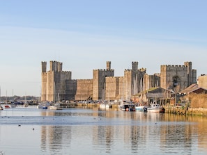 A historic castle with a moat and boats docked in the foreground. - Beech Tree Cottage (Caernarfon)