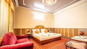 Una habitación de hotel con una cama, una silla roja, una mesita y una alfombra estampada.