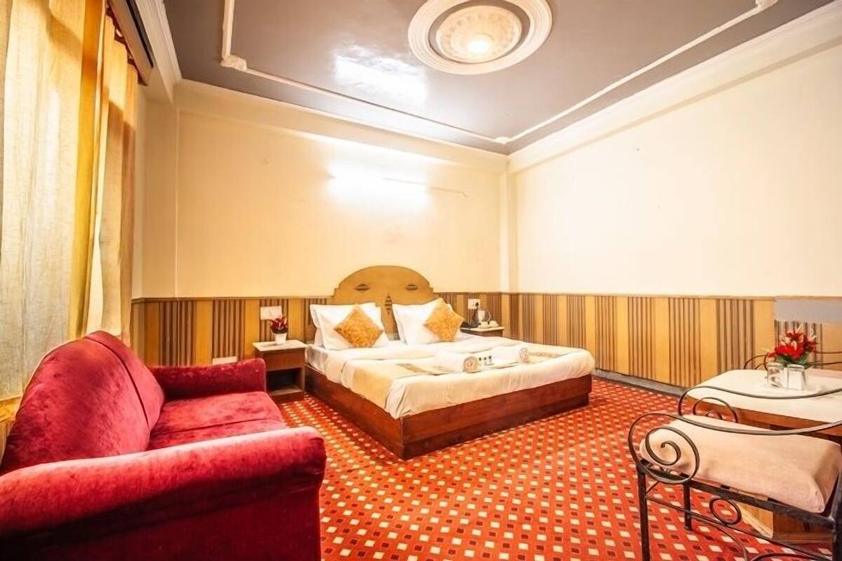 A hotel room with a bed, a red chair, a small table, and a patterned carpet.
