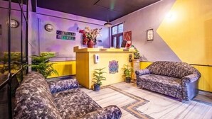 Un vestíbulo de hotel con mostrador de recepción, dos sofás estampados y una pared decorativa.