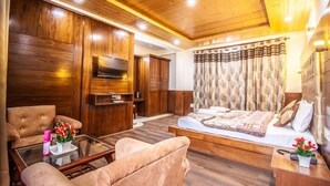 Una habitación con techo de madera, una cama con colcha estampada, un televisor montado en la pared, un sofá y una mesa de centro con un jarrón de flores.