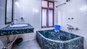 Un baño con lavamanos de mármol, bañera y ventana con ventilador.