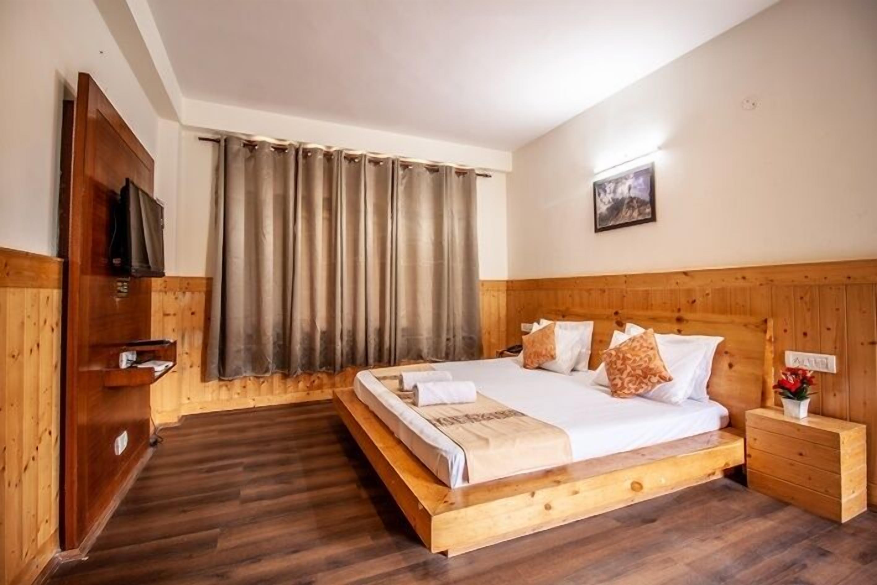 A wooden-paneled room with a bed, a nightstand, a TV, and a window with curtains.