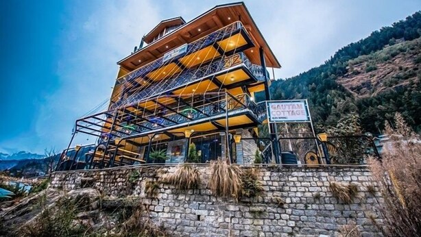 Un edificio de varios pisos con base de piedra y estructura superior de madera, rodeado de un paisaje montañoso.