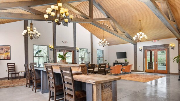 Un vaste espace dédié à la salle à manger, avec une longue table en bois, de nombreuses chaises et des luminaires suspendus.
