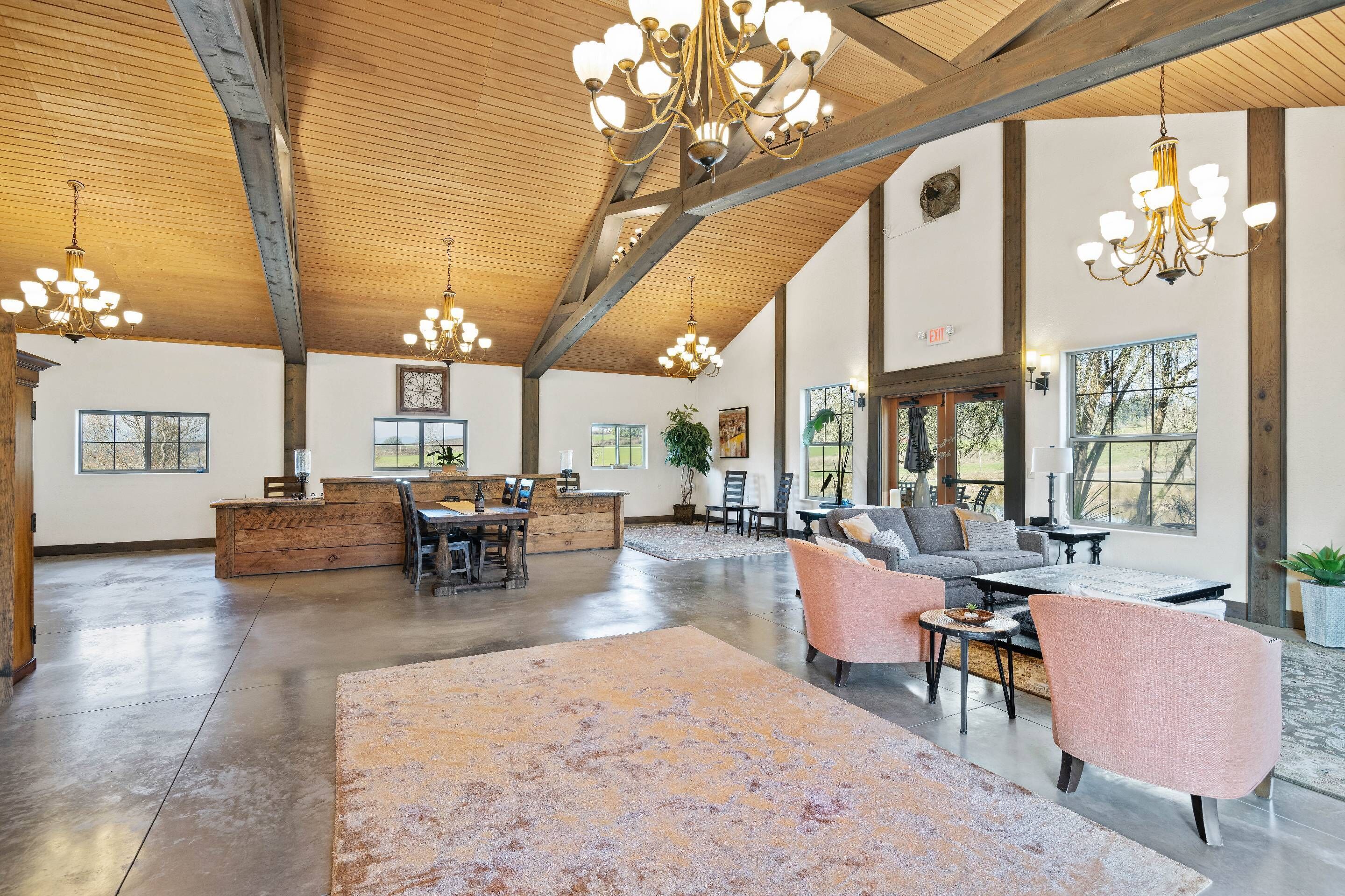 Un'ampia hall con soffitti alti, travi in legno e diversi lampadari. Si trova una reception, un'area salotto con divani e poltrone, e ampie finestre che offrono luce naturale.