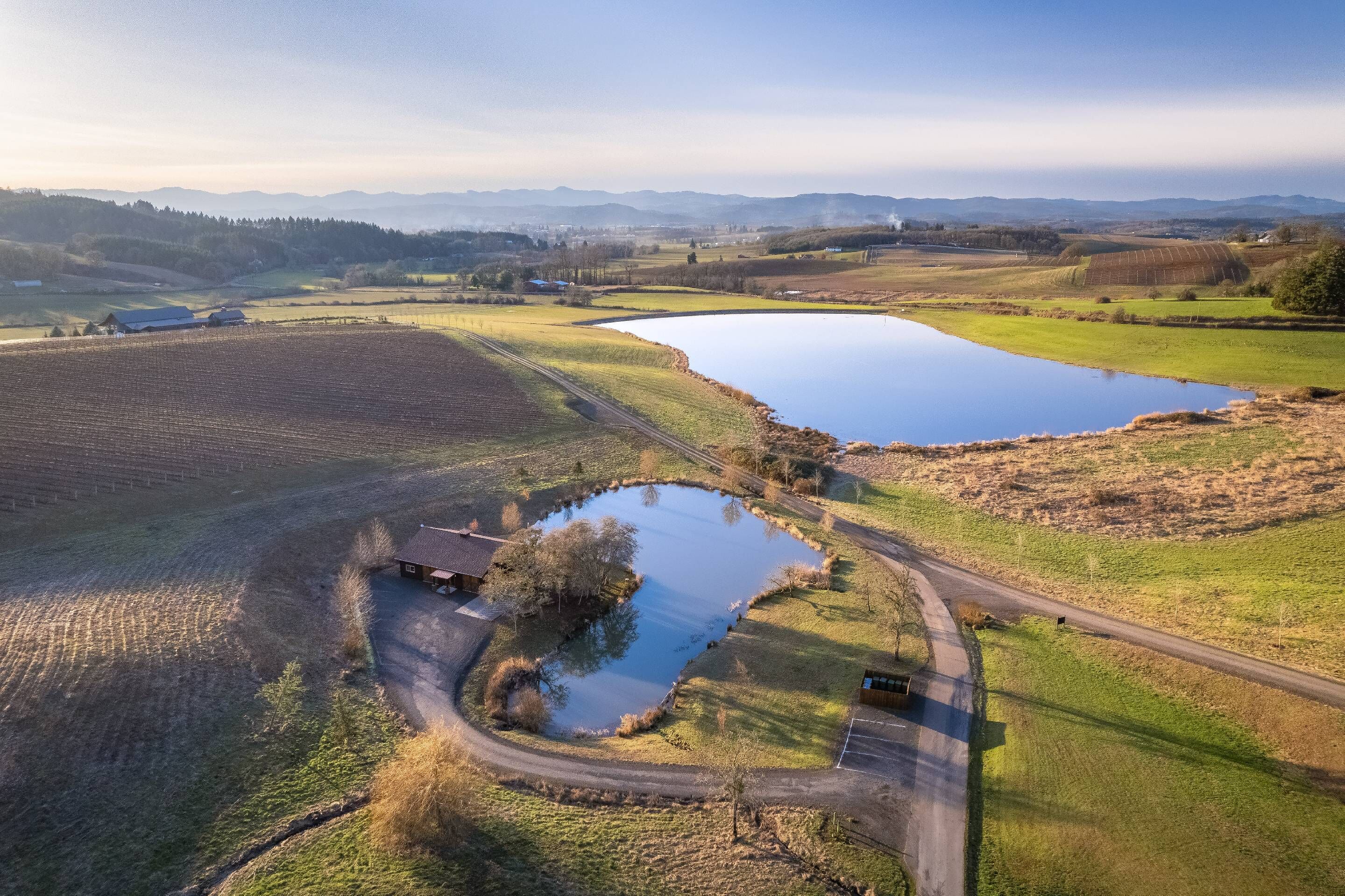 Une vue aérienne d’un paysage rural avec des champs, un étang et un petit bâtiment.