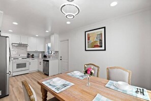 A modern kitchen with white cabinets, stainless steel appliances, and a dining area with a wooden table set for four. - Bright & Peace 3BR, RWC Fresh Remodeled & Spotless (Redwood City)