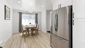 A modern kitchen with white cabinets, a stainless steel refrigerator, and a dining table with chairs. - Bright & Peace 3BR, RWC Fresh Remodeled & Spotless (Redwood City)