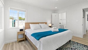 A bedroom with a bed, bedside table, nightstand, and a window with a view of greenery. - Bright & Peace 3BR, RWC Fresh Remodeled & Spotless (Redwood City)