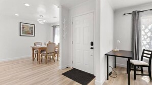 A modern interior with a dining area, a door with a handle, and a small table with a chair. - Bright & Peace 3BR, RWC Fresh Remodeled & Spotless (Redwood City)