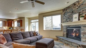 A living room with a stone fireplace, a large sectional sofa, and a dining area in the background. - Fantastic Eagle Crest Home, Resort Pool, Fitness Center, Golf, Pickleball, Fireplace, Quiet Street (Redmond)