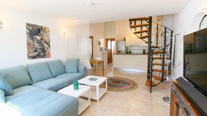 A living room with a sofa, coffee table, and TV. There is a staircase leading to a kitchen with white cabinets and a microwave. - Nice Bungalow next to Denia (Denia)