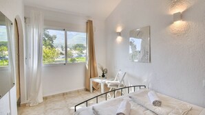 A bedroom with a bed, a desk, and a chair. There is a window with curtains, a painting on the wall, and a view of the outdoors. - Nice Bungalow next to Denia (Denia)