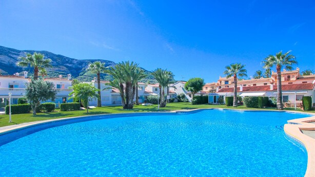 A large, clear swimming pool surrounded by palm trees and buildings with red-tiled roofs. - Nice Bungalow next to Denia (Denia)
