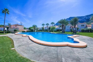 A swimming pool with a unique shape, surrounded by palm trees and houses, with a mountain in the background. - Nice Bungalow next to Denia (Denia)