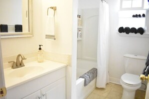 A bathroom with a sink, mirror, shower, toilet, and a towel rack with towels. - Eclectic West Riverside Apt | 6 min to Audobon Zoo (New Orleans)