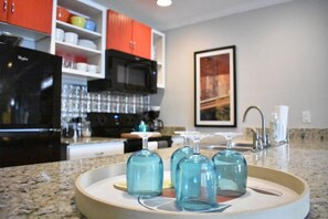 A kitchen with a granite countertop, a microwave, and a coffee machine. There are four blue glasses on a tray. - Eclectic West Riverside Apt | 6 min to Audobon Zoo (New Orleans)