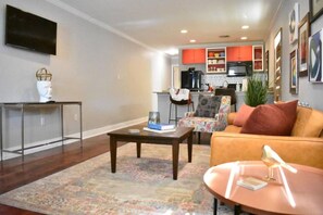 A living room with a sofa, coffee table, and a rug. There is a kitchen in the background with cabinets and a microwave. - Eclectic West Riverside Apt | 6 min to Audobon Zoo (New Orleans)