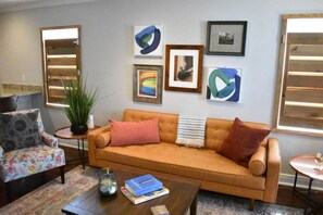 A living room with a sofa, armchair, and coffee table. There are framed artworks on the wall and a potted plant on a side table. - Eclectic West Riverside Apt | 6 min to Audobon Zoo (New Orleans)