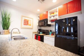 A kitchen with granite countertops, a stainless steel sink, a black refrigerator, and red cabinets.