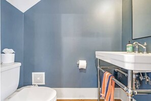 A bathroom with a white toilet, a white sink with a towel, and a blue wall.